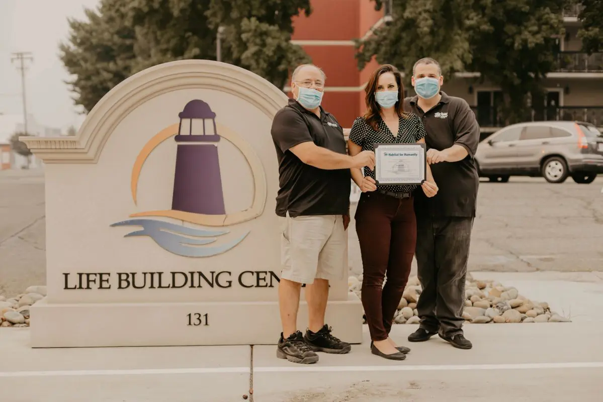 Three people standing in front of a sign that says life building center.