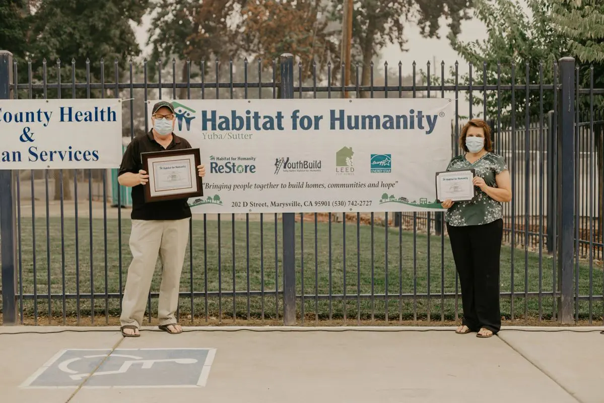 Two people standing in front of a fence with plaques.