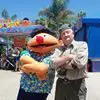 A man posing next to a mascot at an amusement park.