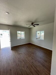 Empty living room with hardwood floors and a ceiling fan.