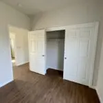 An empty room with white closets and hardwood floors.