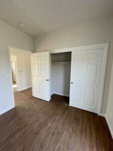 An empty room with white closets and hardwood floors.
