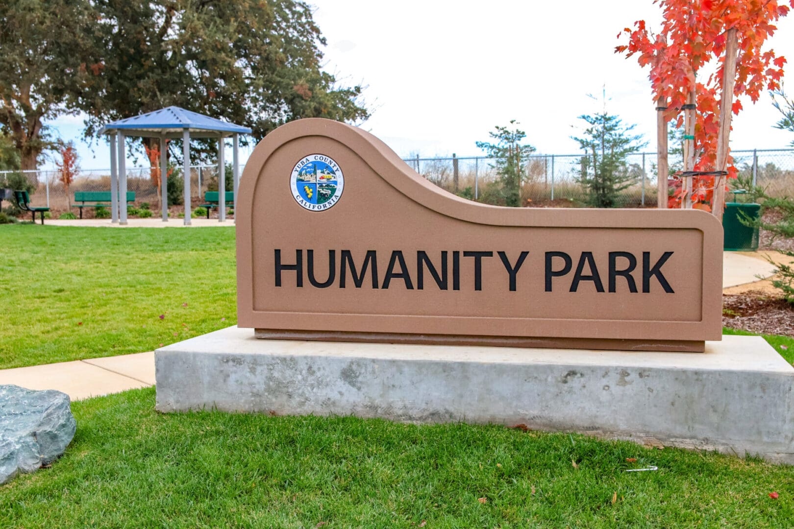 A sign that says humanity park in front of a grassy area.