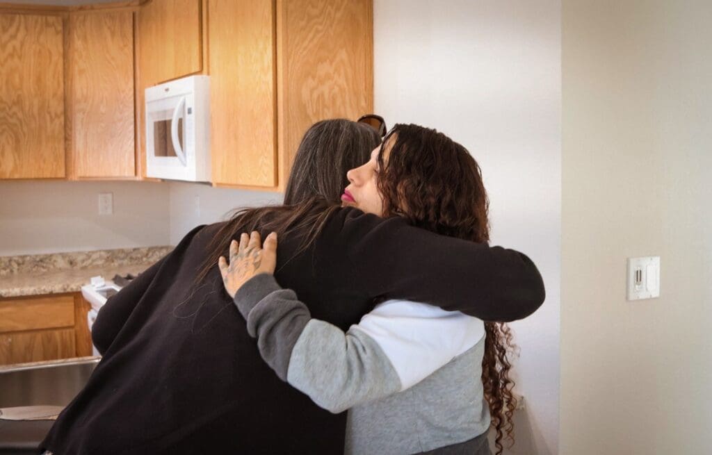 Two women embrace in a kitchen.