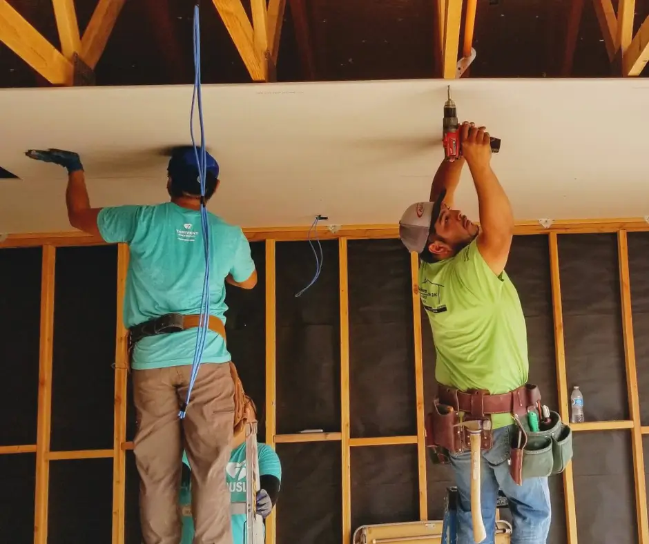 Workers installing drywall ceiling with power tools.